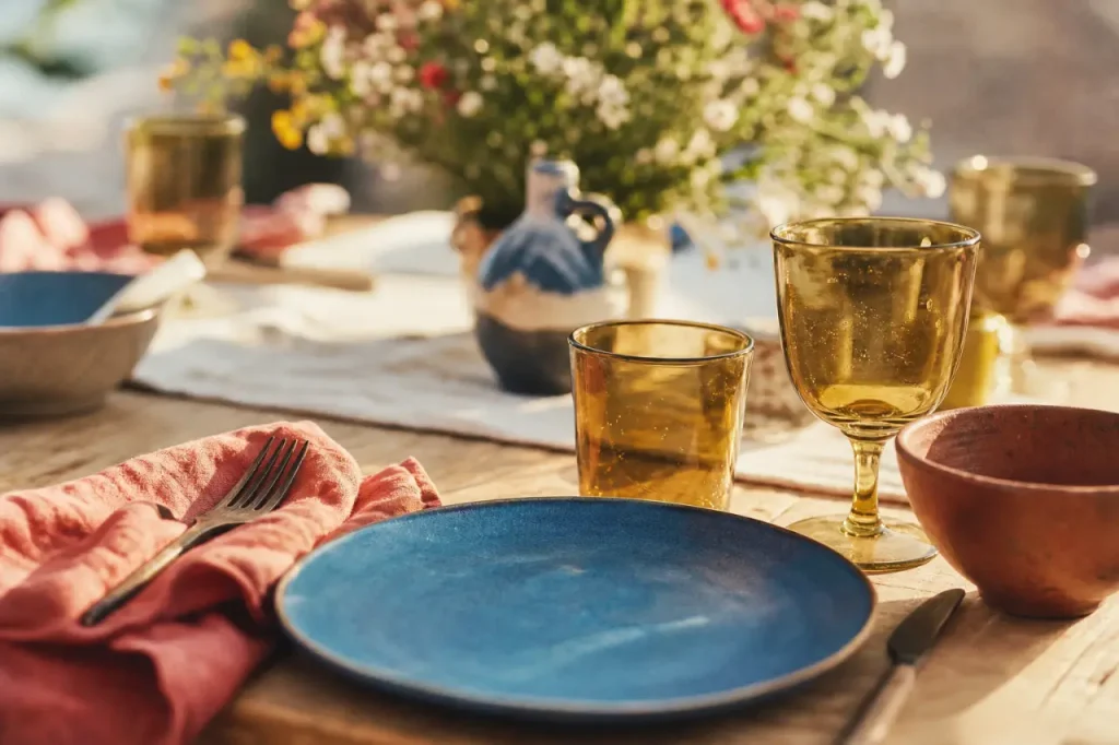 Vaisselle coloré bleu océan, terracotta et verres ambrés sur table en bois