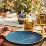 Vaisselle coloré bleu océan, terracotta et verres ambrés sur table en bois